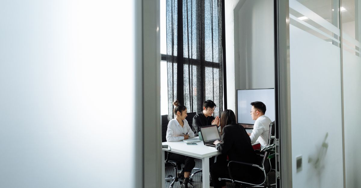Group collaborating in a well-lit office room with large windows, discussing business strategies.