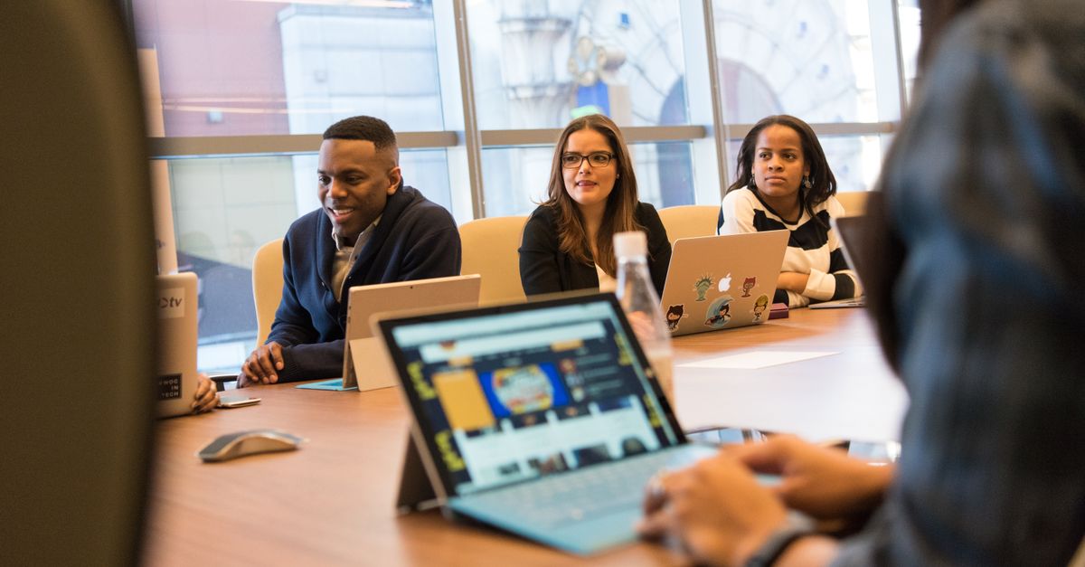 A diverse group of professionals working together on laptops in a modern office meeting room.