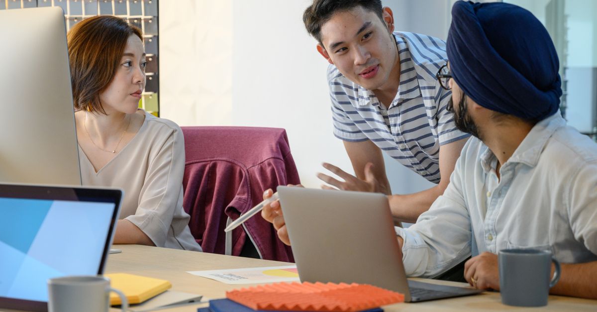 A diverse team engaged in a business meeting discussing ideas with laptops.