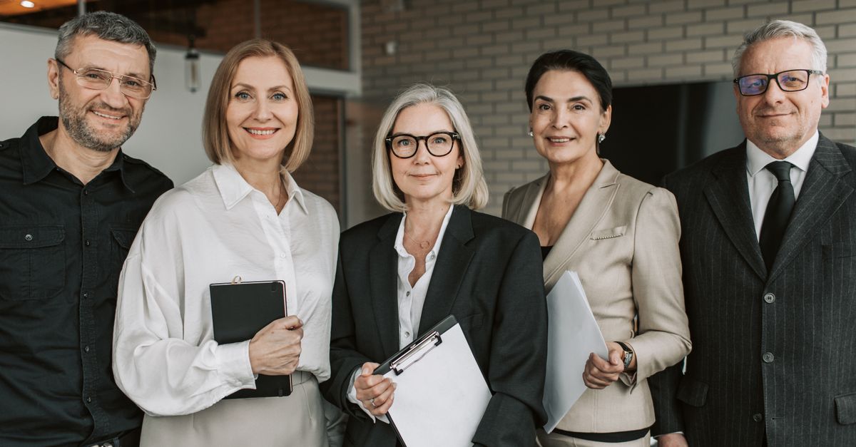 A diverse team of senior business professionals posing confidently indoors.