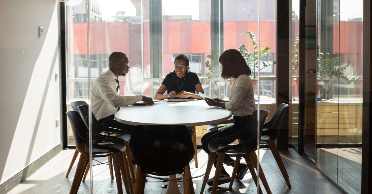 Three professionals collaborating in a modern office boardroom setting during daylight.