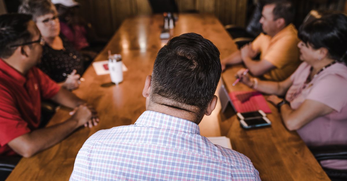 A business meeting with a diverse team discussing around a wooden table in an office setting.