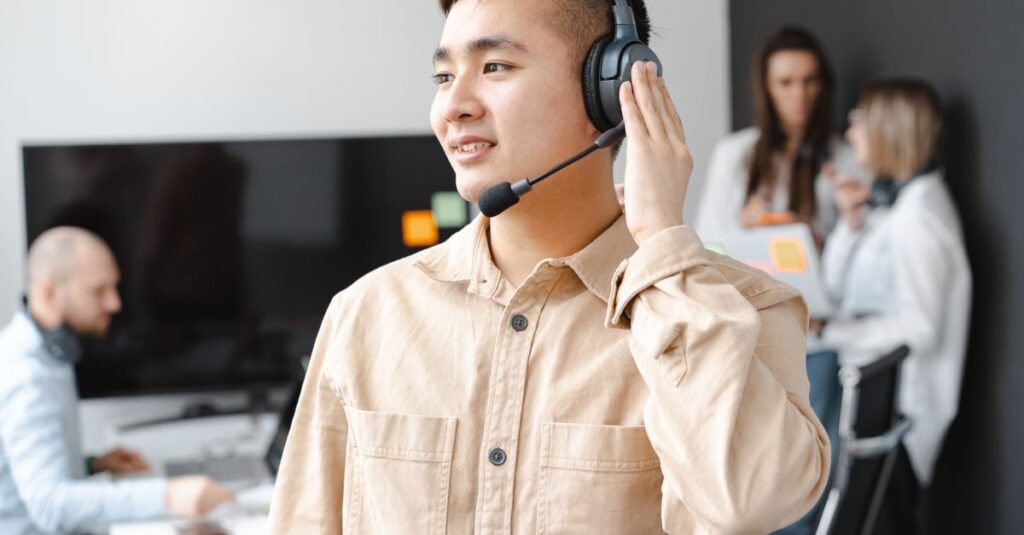 Asian man in beige shirt smiling with headset in modern office setting.