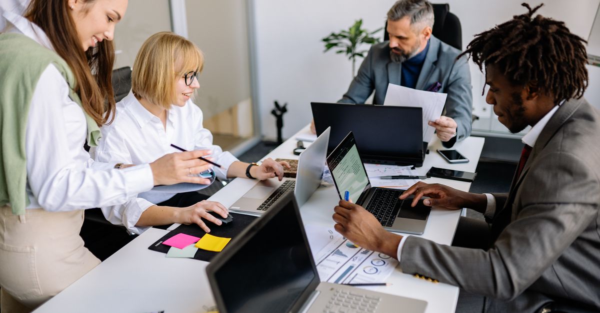 A diverse team collaborates in a modern office setting with laptops and documents.