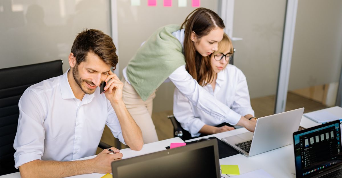 Three professionals engaged in teamwork at a conference table with laptops and notes.