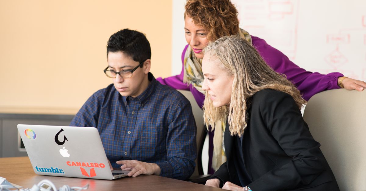 Team of three people collaborating on a laptop in an office setting.