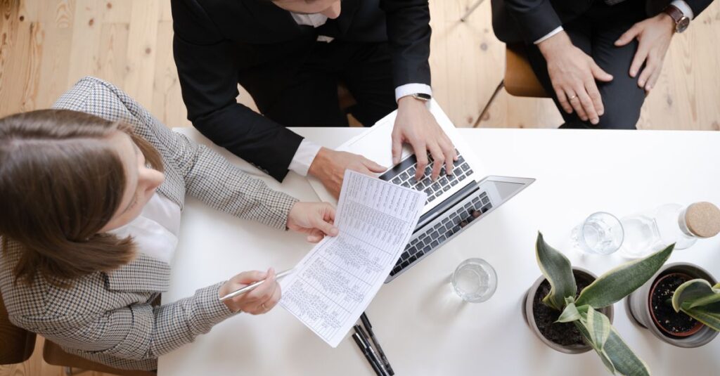 Overhead view of colleagues collaborating at a desk with laptop and documents in a business meeting.