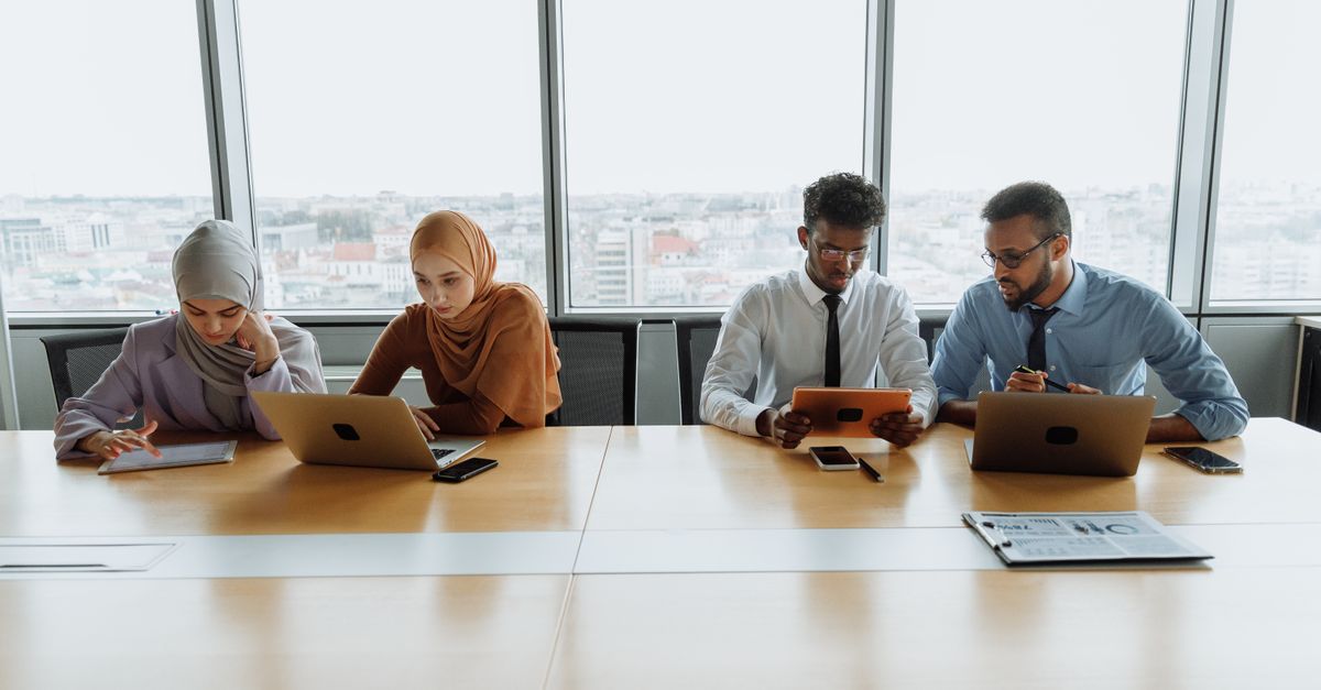 A diverse group of colleagues working together using laptops and tablets in a modern office setting.