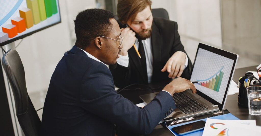 Two business professionals working on growth charts using laptop in an office setting.