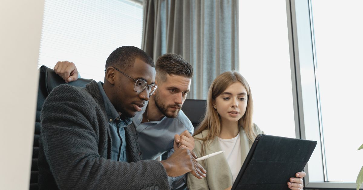 Team of three diverse professionals working on a project with a tablet in a modern office setting.