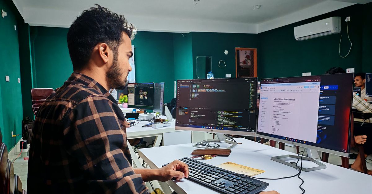 Software developer coding on dual monitors in a well-lit modern office, focused and engaged.