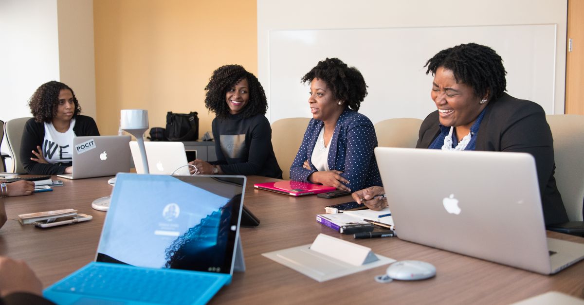 Group of women engaged in a collaborative meeting at an office table with laptops.