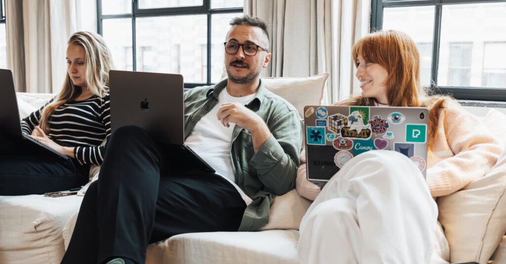Three adults working on laptops in a casual office environment, discussing ideas.