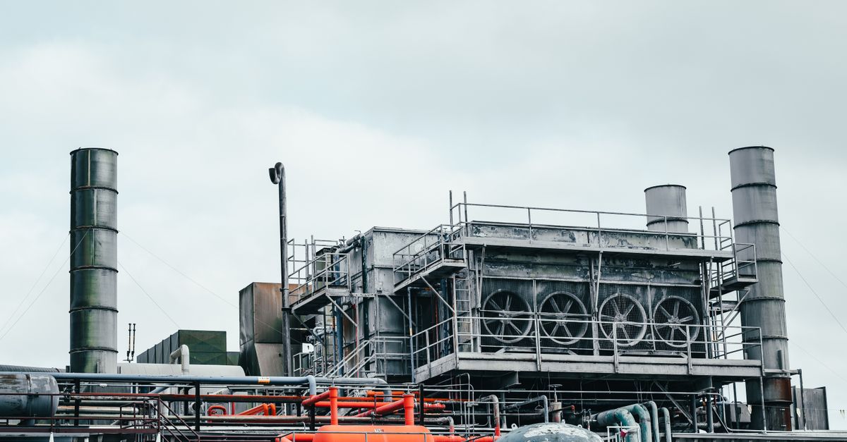 Industrial factory with metal pipes and special equipment surrounded with fences located against cloudy sky on street with power lines in town