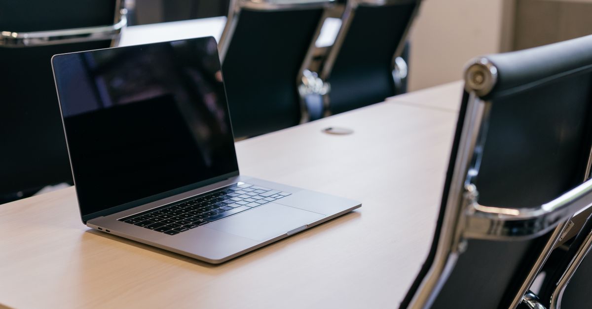 Open laptop on a wooden conference table with stylish black chairs in a modern office setting.