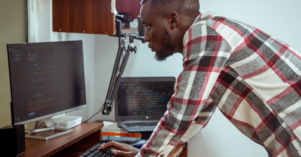 Focused IT specialist in casual attire working at a computer in a modern office setting.