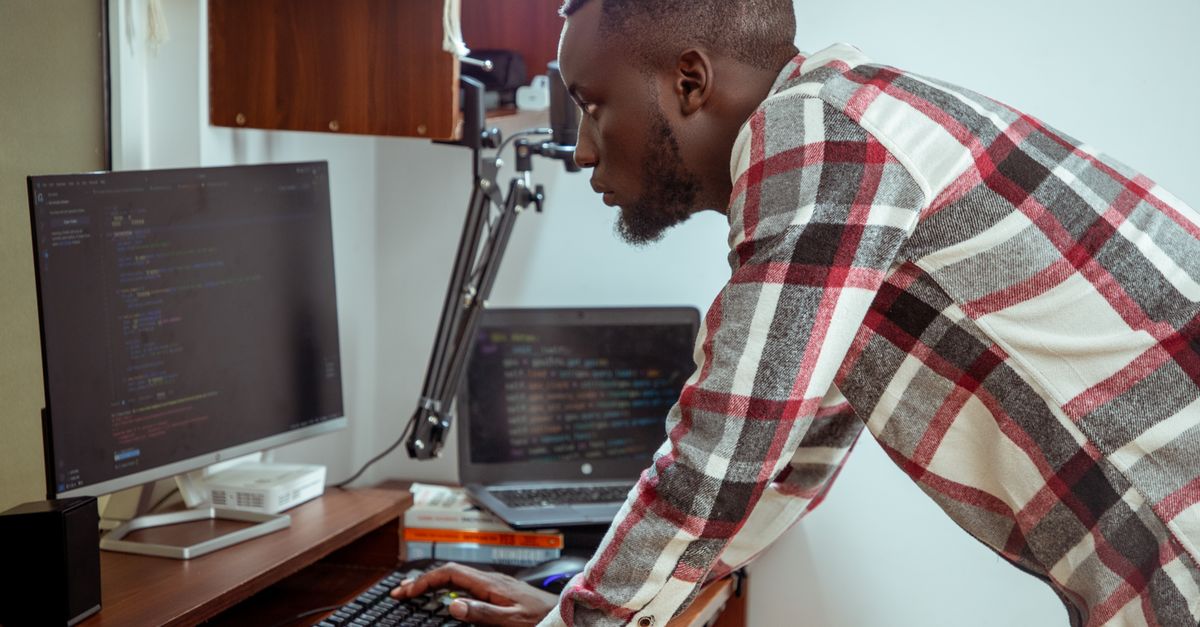 Focused IT specialist in casual attire working at a computer in a modern office setting.