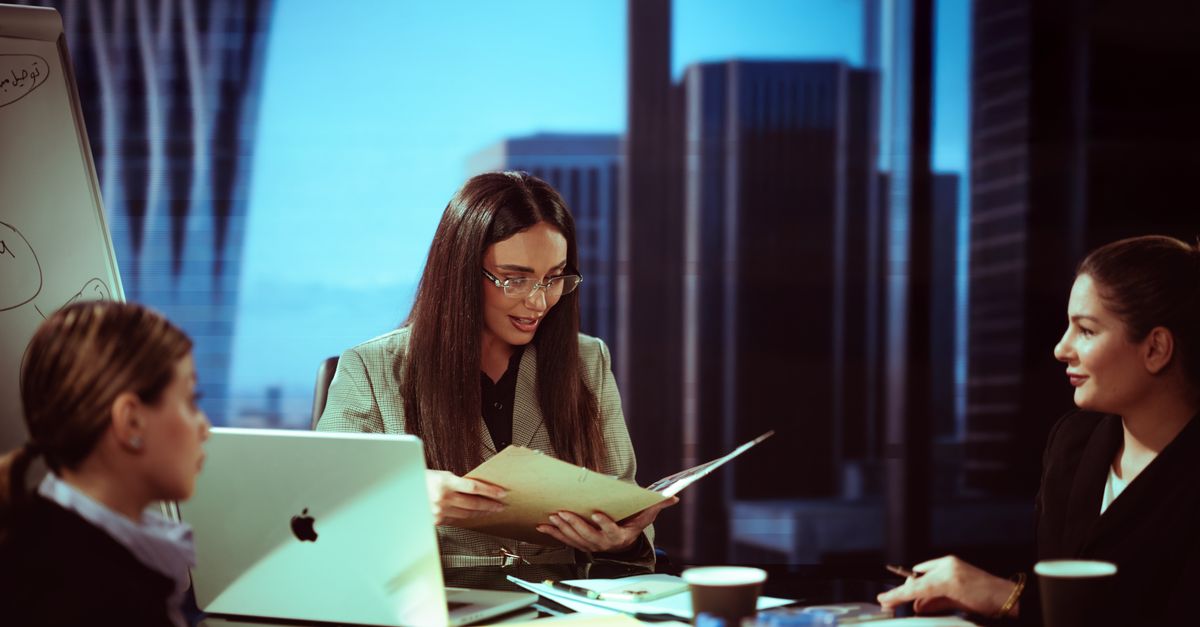 Three businesswomen engaged in a meeting at a Baghdad office with a city view.