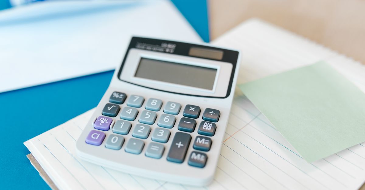 A white calculator on a stack of lined paper with a blue folder, capturing an office setting.