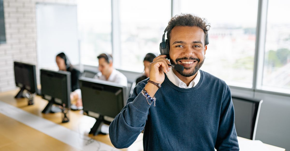 Cheerful male call center agent with headset in a bright office environment.