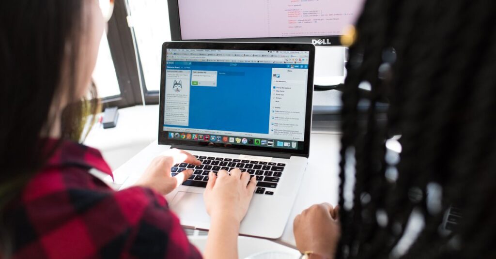 Two women working together on a laptop in a bright, modern office setting.
