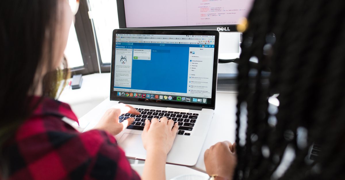 Two women working together on a laptop in a bright, modern office setting.