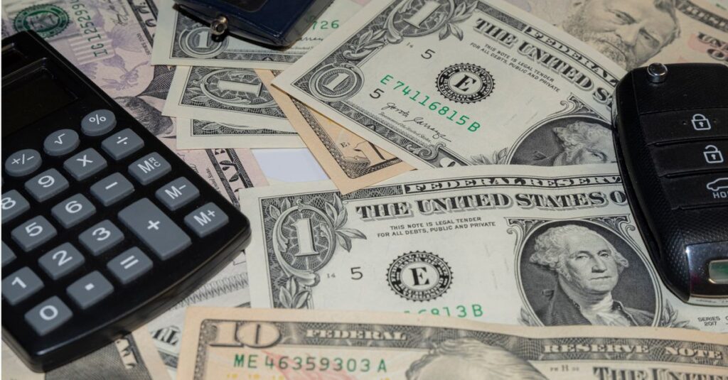 Close-up of various US banknotes, calculator, and car key illustrating finance concept.