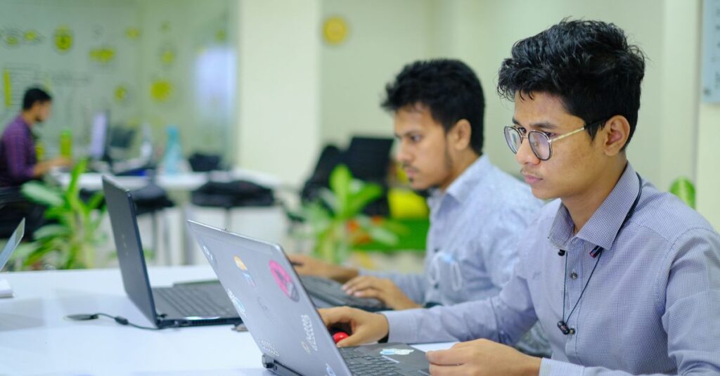 Two young professionals working on laptops in a vibrant and modern office setting.
