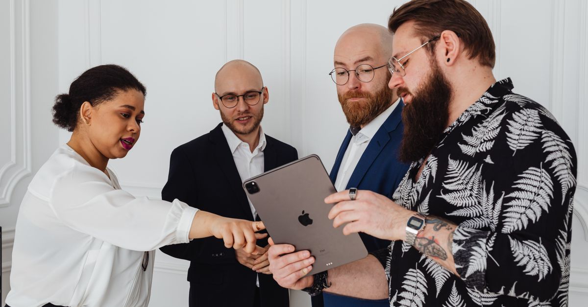 A group of diverse professionals discussing a project using a tablet in a modern office setting.