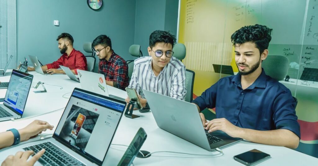 Group of young professionals working together in a modern office setting, using laptops and technology.