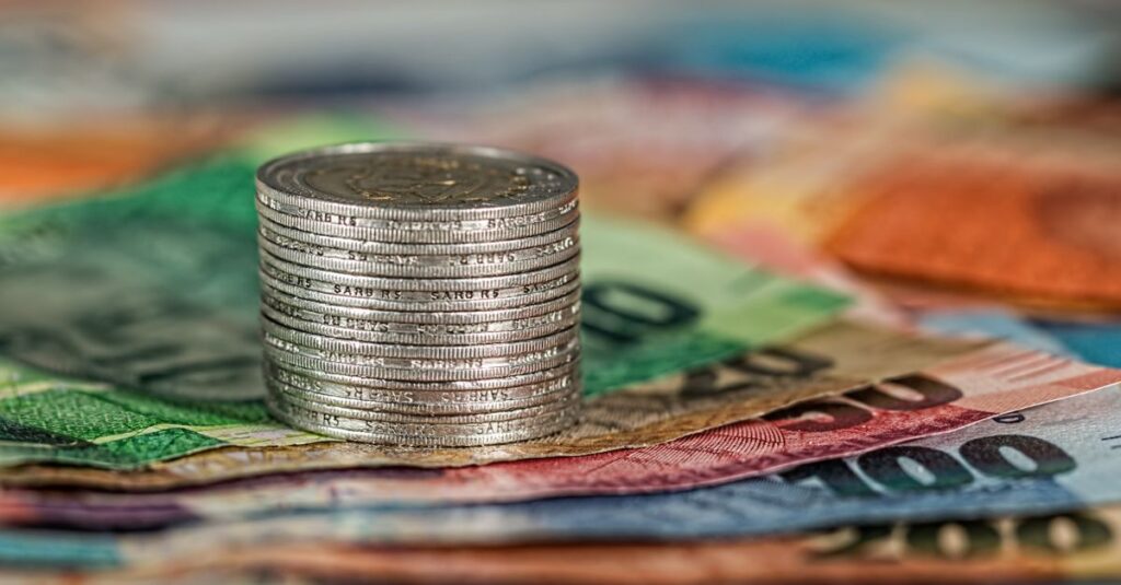 A stack of coins on top of various colored banknotes, symbolizing finance and currency.