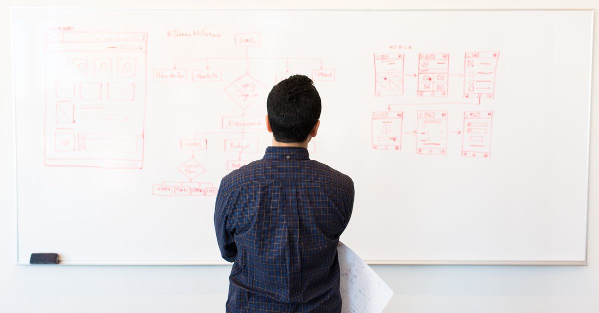 Man analyzing design flowchart on whiteboard in a professional office setting.