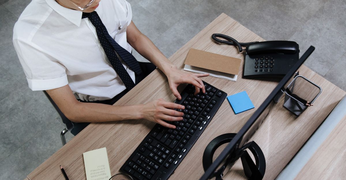 Asian man in business attire typing on a keyboard at a modern office desk.