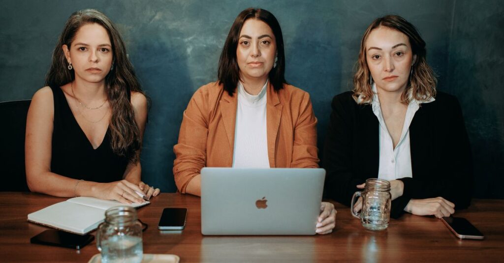 Three serious women in formal wear at a business meeting with laptops and notebooks.