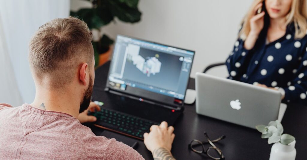 Two professionals working on laptops, engaging in a collaborative office environment.