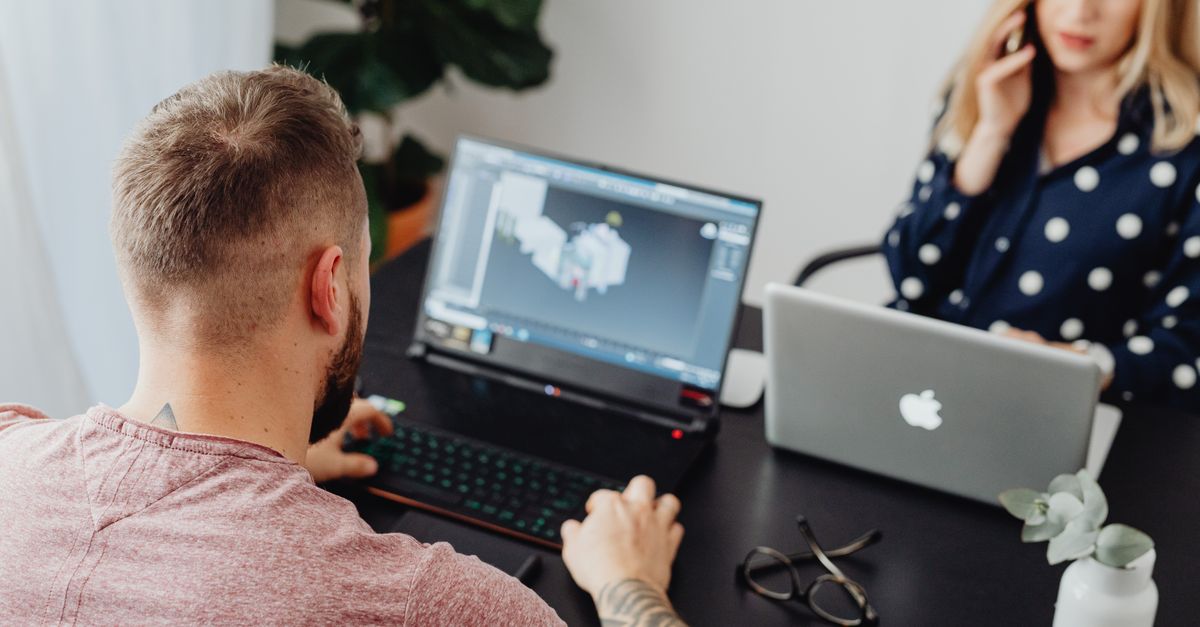 Two professionals working on laptops, engaging in a collaborative office environment.