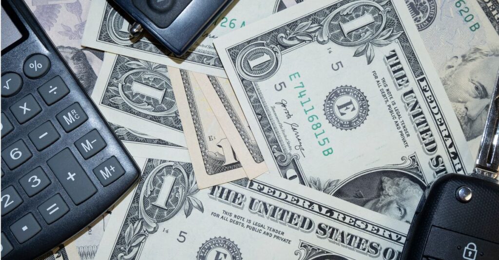 An arrangement of US dollar bills, car keys, and a calculator representing finance and investment concepts.