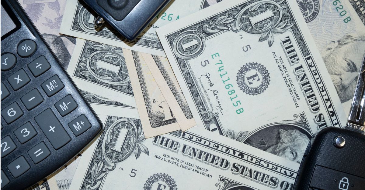 An arrangement of US dollar bills, car keys, and a calculator representing finance and investment concepts.