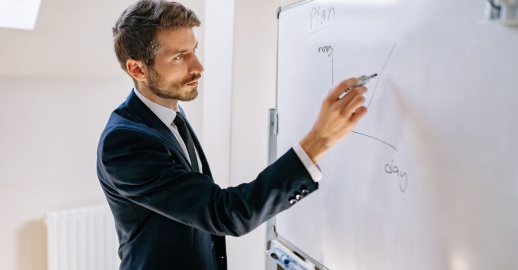 Executive in suit writing on whiteboard, explaining business graph.