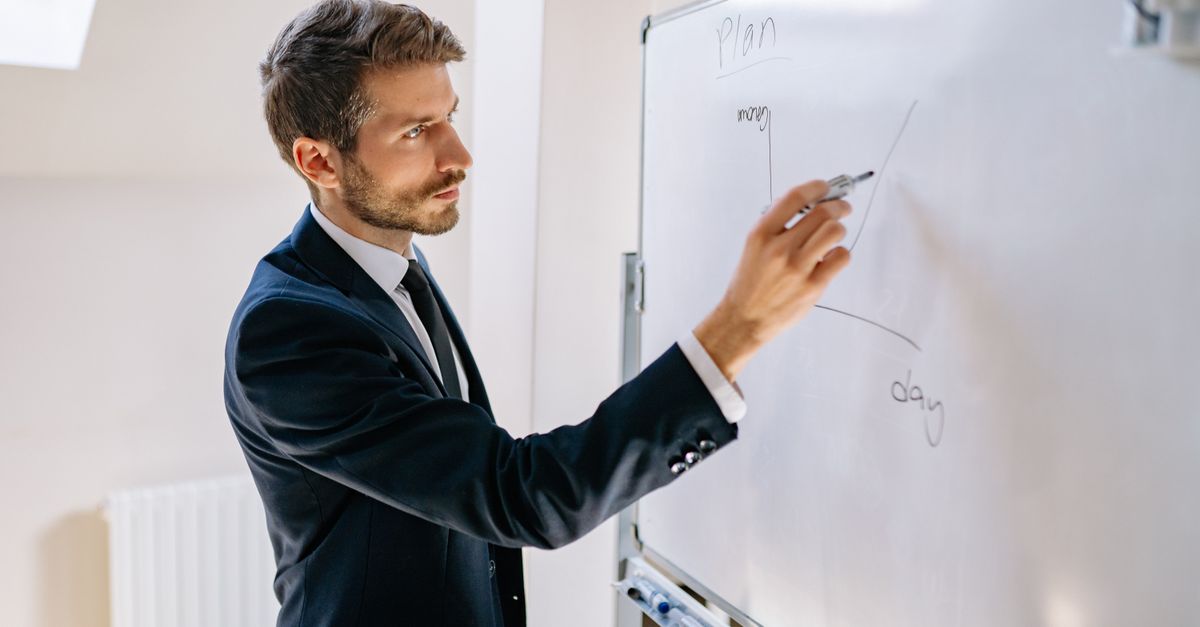 Executive in suit writing on whiteboard, explaining business graph.