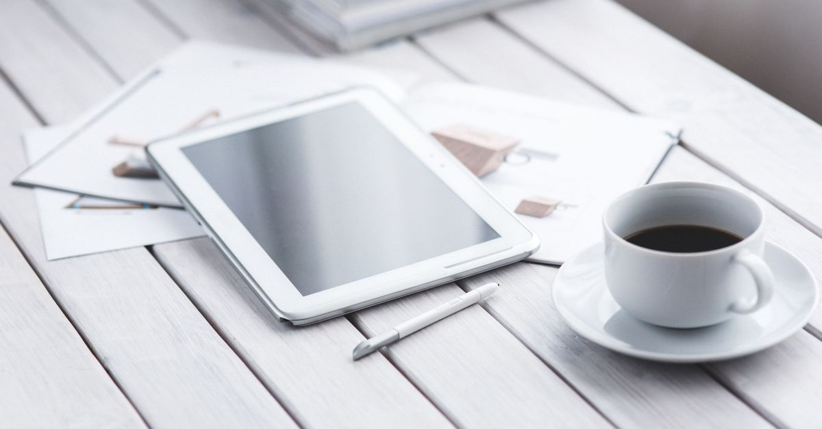 White tablet with stylus and coffee cup on modern office desk setup.