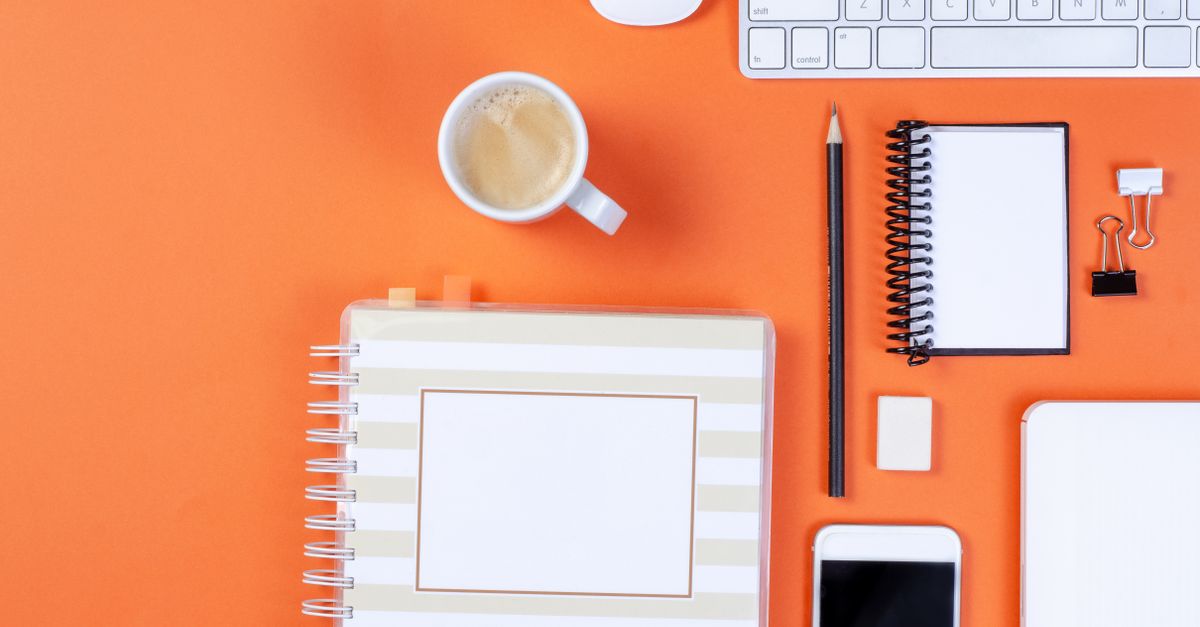 Flat lay of office items on an orange background including keyboard, coffee, and smartphone.