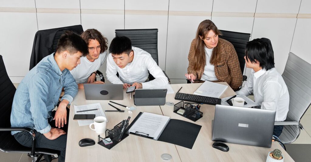 A diverse group of colleagues working together in an office setting with laptops and documents.