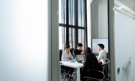 Group collaborating in a well-lit office room with large windows, discussing business strategies.