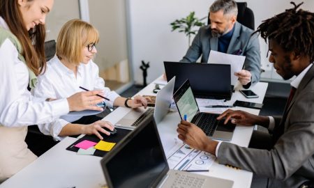 A diverse team collaborates in a modern office setting with laptops and documents.