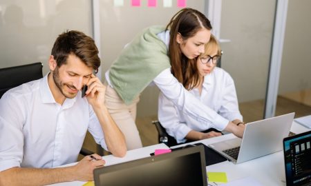 Three professionals engaged in teamwork at a conference table with laptops and notes.