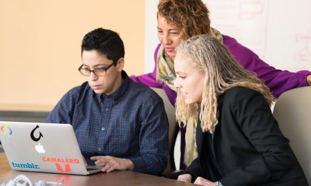 Team of three people collaborating on a laptop in an office setting.
