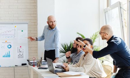A group of professionals engaged in a business meeting, discussing financial graphs on a whiteboard.