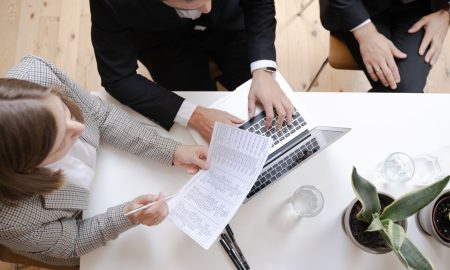Overhead view of colleagues collaborating at a desk with laptop and documents in a business meeting.