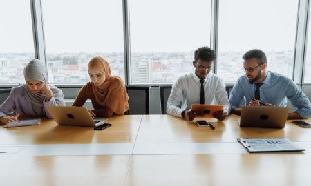 A diverse group of colleagues working together using laptops and tablets in a modern office setting.